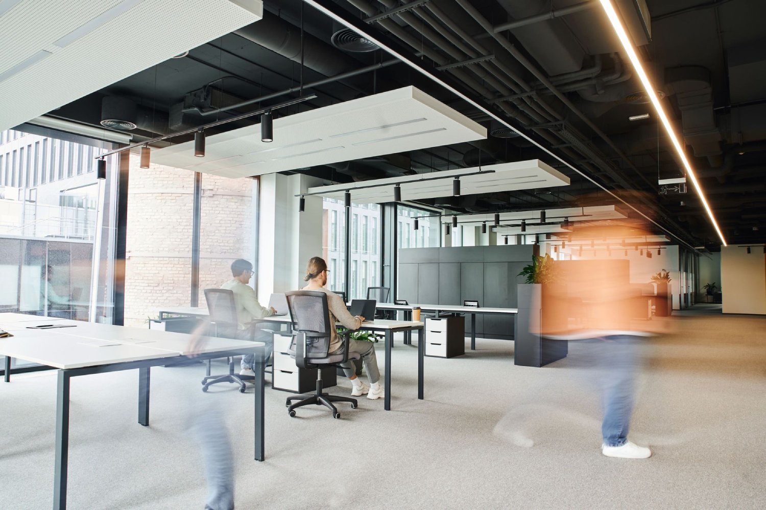 A modern office space with workers at desks and blurred motion of people walking.