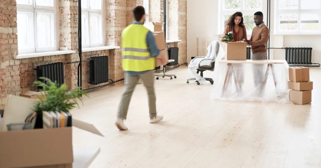 A man and woman are collaborating to move cardboard boxes in a modern office setting.