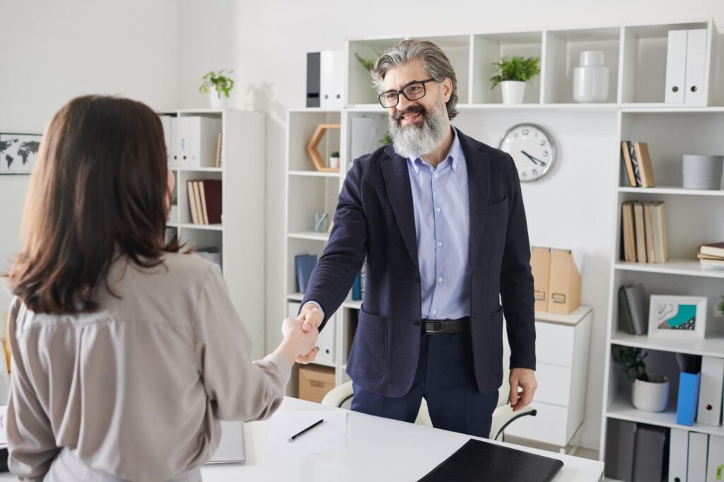 A man and a woman shaking hands in a modern office setting.